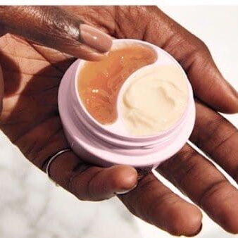 A person holding a jar of cream on their hand.